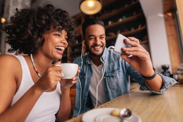 Young-man-and-woman-watching-video-on-phone-at-coffee-shop